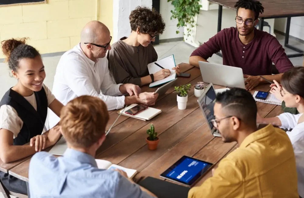 Equipo de trabajo reunido alrededor de una mesa de madera con portátiles y cuadernos