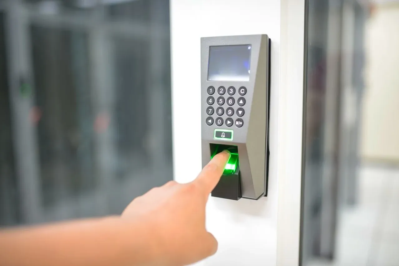 Dedo de una persona sobre el lector de huella de un control de acceso con teclado numérico en una puerta de oficina
